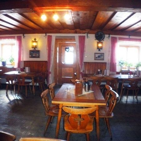 Gemütliches, rustikales Restaurant mit Holzbalken, Tischen und hellen Vorhängen