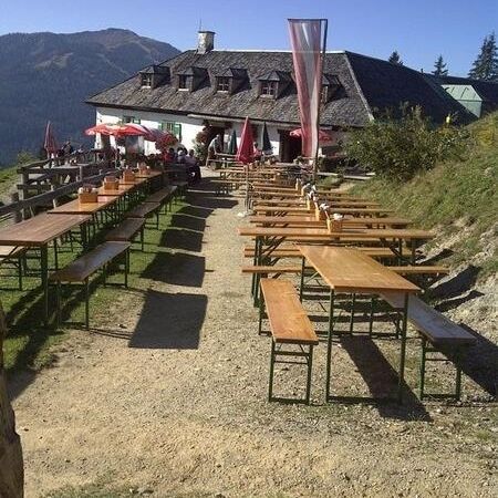 Ein sonniges Außenrestaurant mit Picknicktischen und Sonnenschirmen aus Holz, umgeben von Bergen und Grün