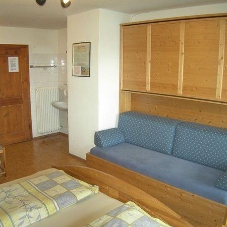 Gemütliches Zimmer mit einem Doppelbett, blauem Sofa, Holzmöbeln und eigenem Bad