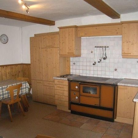 Gemütliche Küche mit Holzschränken, einem rustikalen Tisch und einem orangefarbenen Herd mit einer gekachelten Aufkantung und einem Spülbecken aus Edelstahl