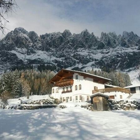 Ein schneebedecktes Chalet am Fuße majestätischer Felsen, umgeben von immergrünen Bäumen unter einem wolkenverhangenen Himmel