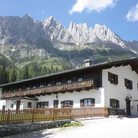 Eine charmante Berghütte mit Holzbalkon vor der Kulisse majestätischer, schroffer Berge unter strahlend blauem Himmel