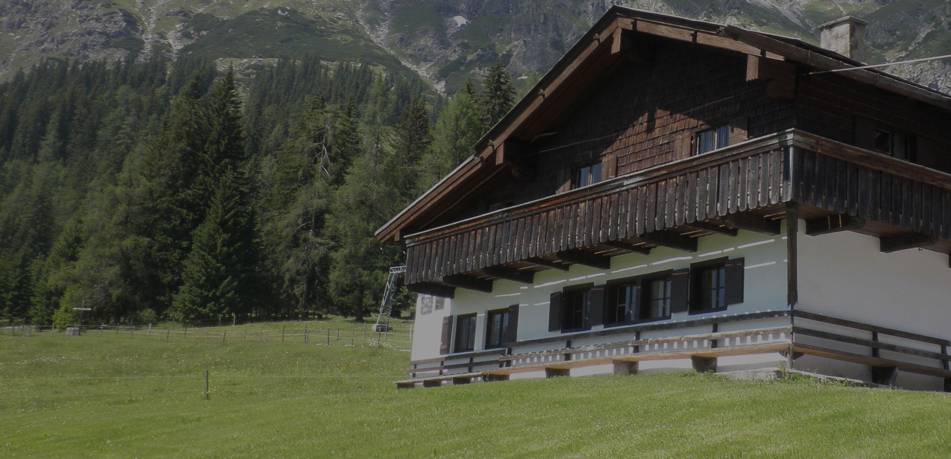 Ein rustikales Holzchalet, eingebettet in saftig grünes Gras, mit hoch aufragenden felsigen Bergen im Hintergrund