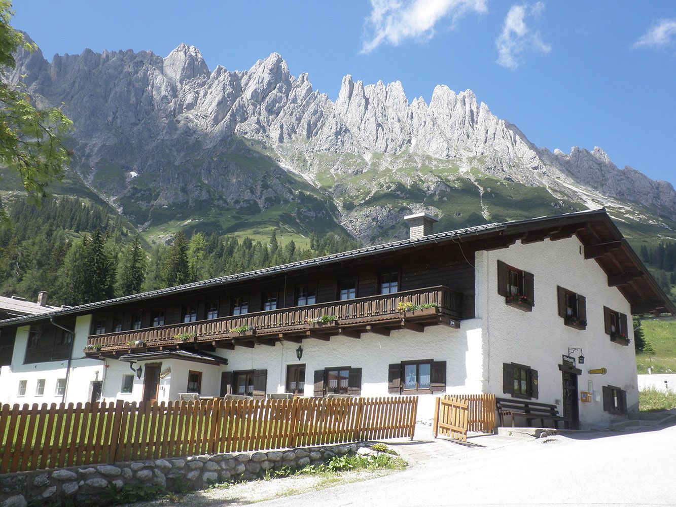 Ein rustikales Holzchalet, eingebettet in saftig grünes Gras, mit hoch aufragenden felsigen Bergen im Hintergrund
