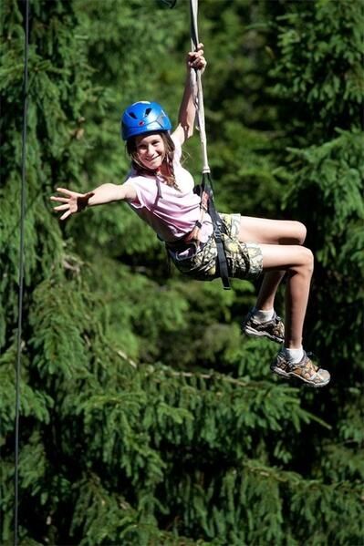 Ein Kind mit blauem Helm hängt an einer Leine im Wald und streckt die Arme aus