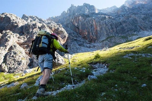 Ein Wanderer steigt, ausgerüstet mit Trekkingstöcken und Rucksack, einen felsigen Pfad hinauf
