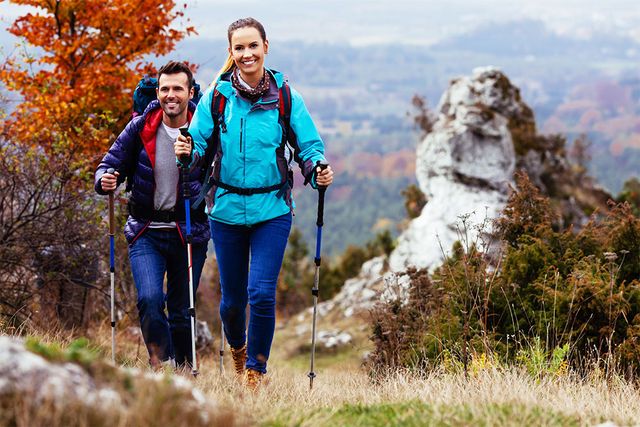 Zwei Wanderer steigen mit Trekkingstöcken und Rucksäcken ausgerüstet einen grasbewachsenen Pfad hinauf