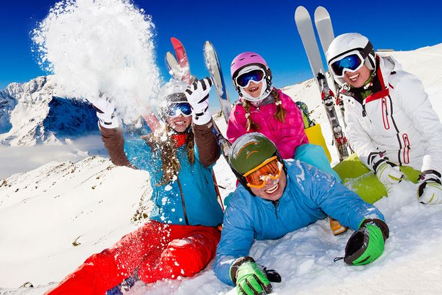 Eine Gruppe von fünf Skifahrern, die fröhlich im Schnee spielen, mit den Skiern im Hintergrund und einem klaren blauen Himmel darüber